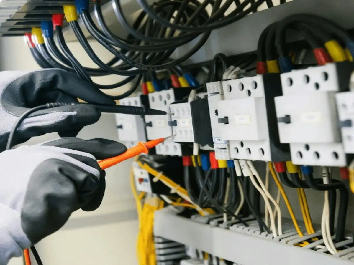 A gloved electrician testing a contactor panel with a multimeter